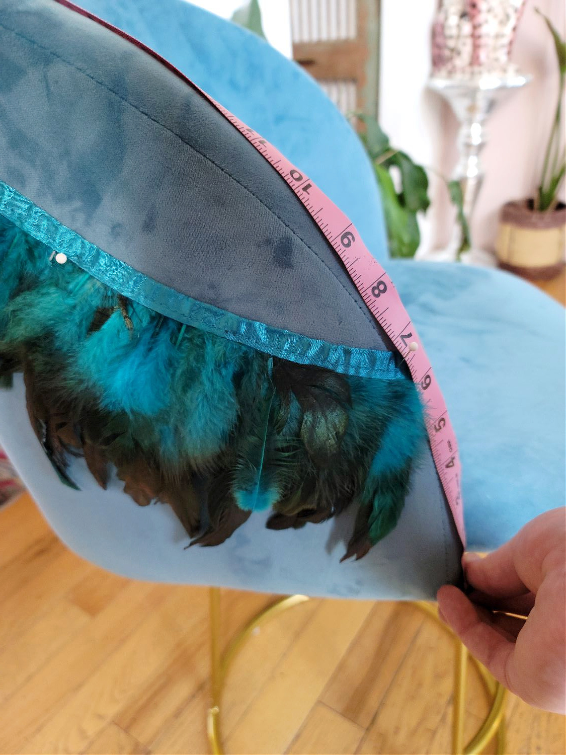 DIY Counter Stools by popular Colorado home design blog, Eclectic Twist: image of blue, black, and green feather trim pinned to a blue fabric counter stool and a woman measuring the back of the counter stool with a pink sewing measuring tape.