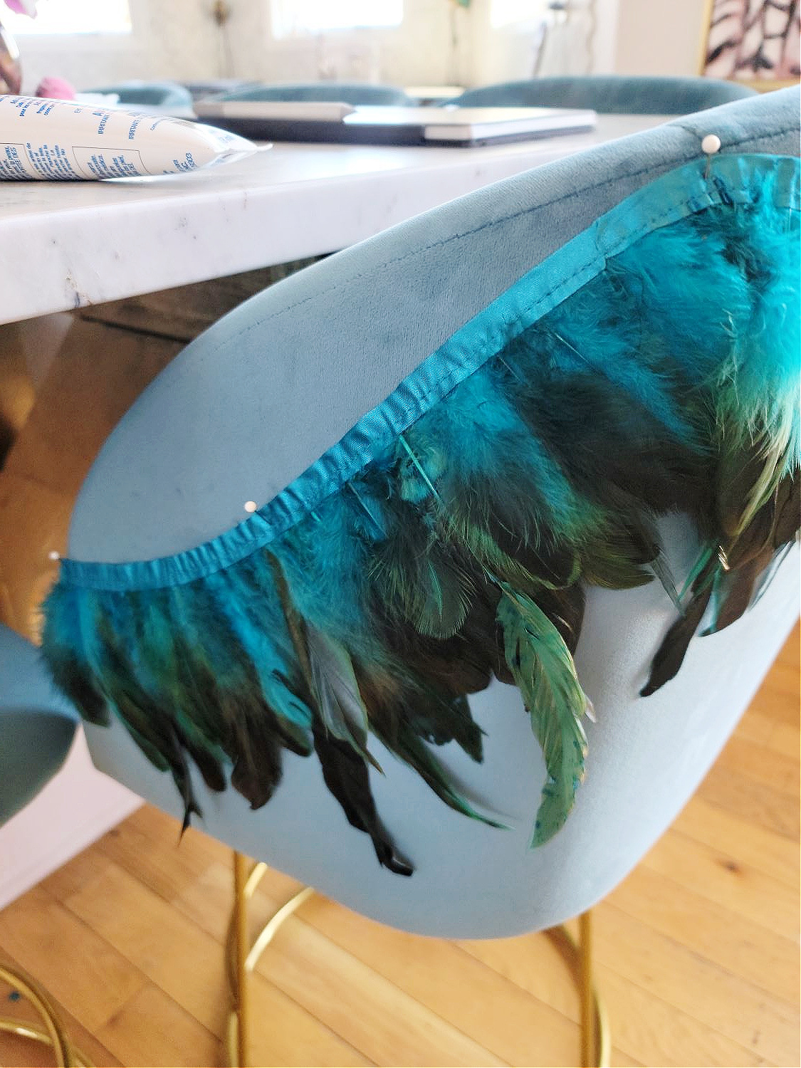 DIY Counter Stools by popular Colorado home design blog, Eclectic Twist: image of blue, green, and black feather trim pinned to the back of a blue fabric counter stool.