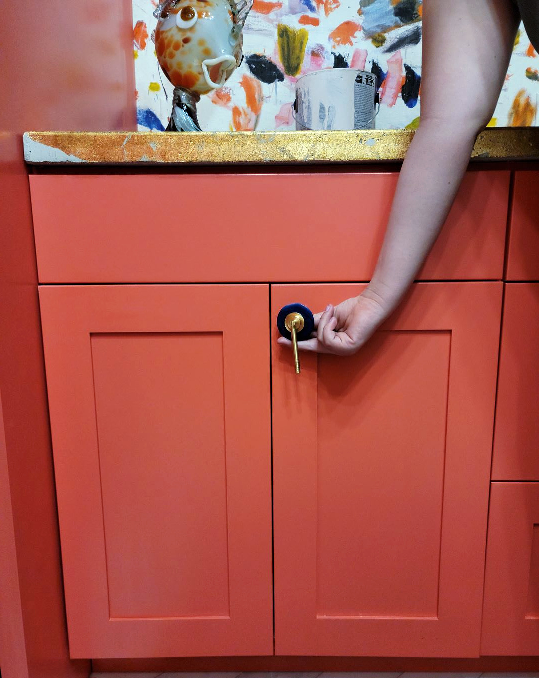 Wallpaper Installation by popular CO home design blog: image of a laundry room with fold counter tops, coral pink cabinets, and paint splatter wallpaper. 