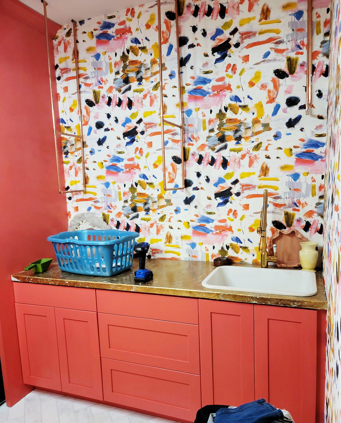 Wallpaper Installation by popular CO home design blog: image of a laundry room with coral pink cabinets and paint splatter wallpaper. 