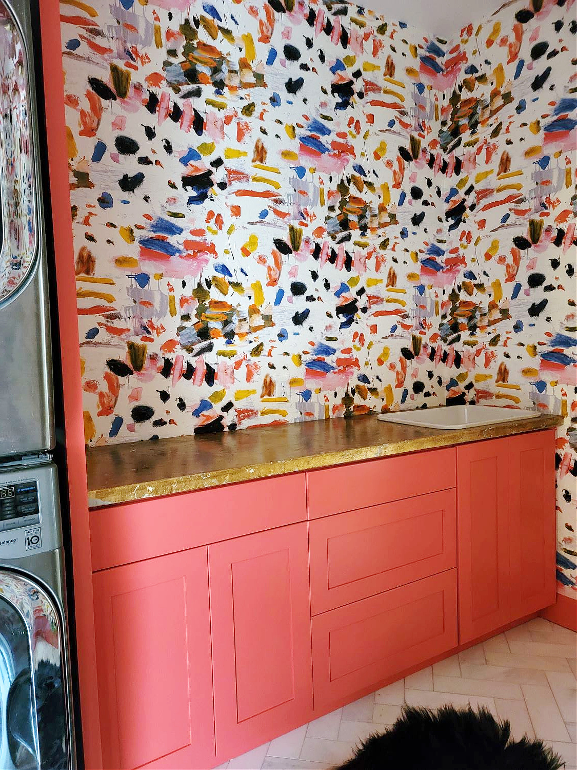 Wallpaper Installation by popular CO home design blog: image of a laundry room with coral pink cabinets, white marble flooring and paint splatter wallpaper. 