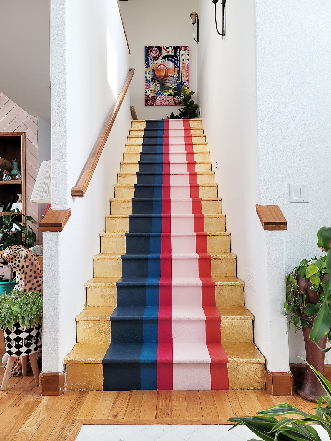 Staircase Makeover by popular CO home design blog, Eclectic Twist: image of a wooden staircase with navy blue, cobalt blue, dark pink, light pink, orange stripes and gold leafing on it. 