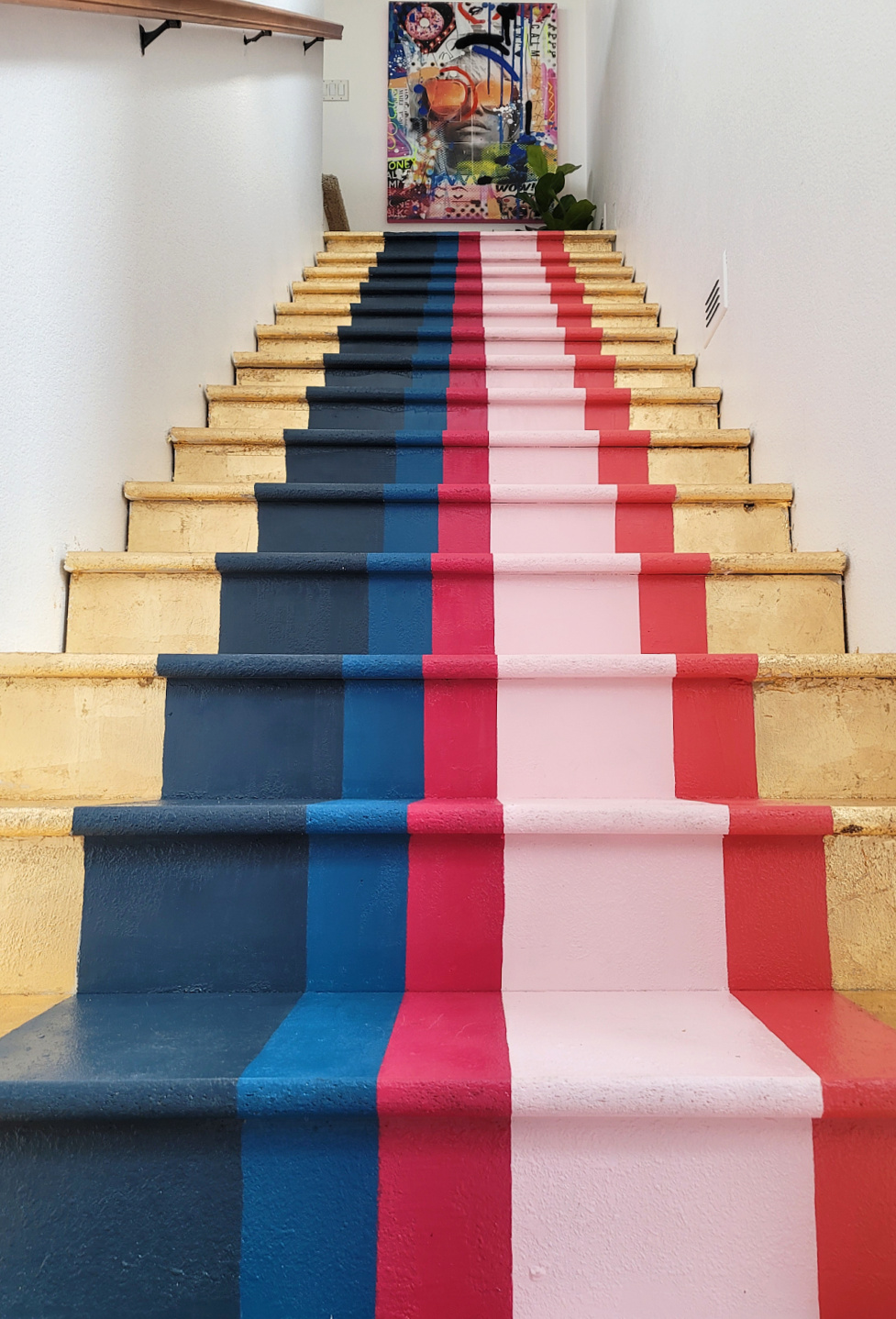 Staircase Makeover by popular CO home design blog, Eclectic Twist: image of a wooden staircase with navy blue, cobalt blue, dark pink, light pink, orange stripes and gold leafing on it. 