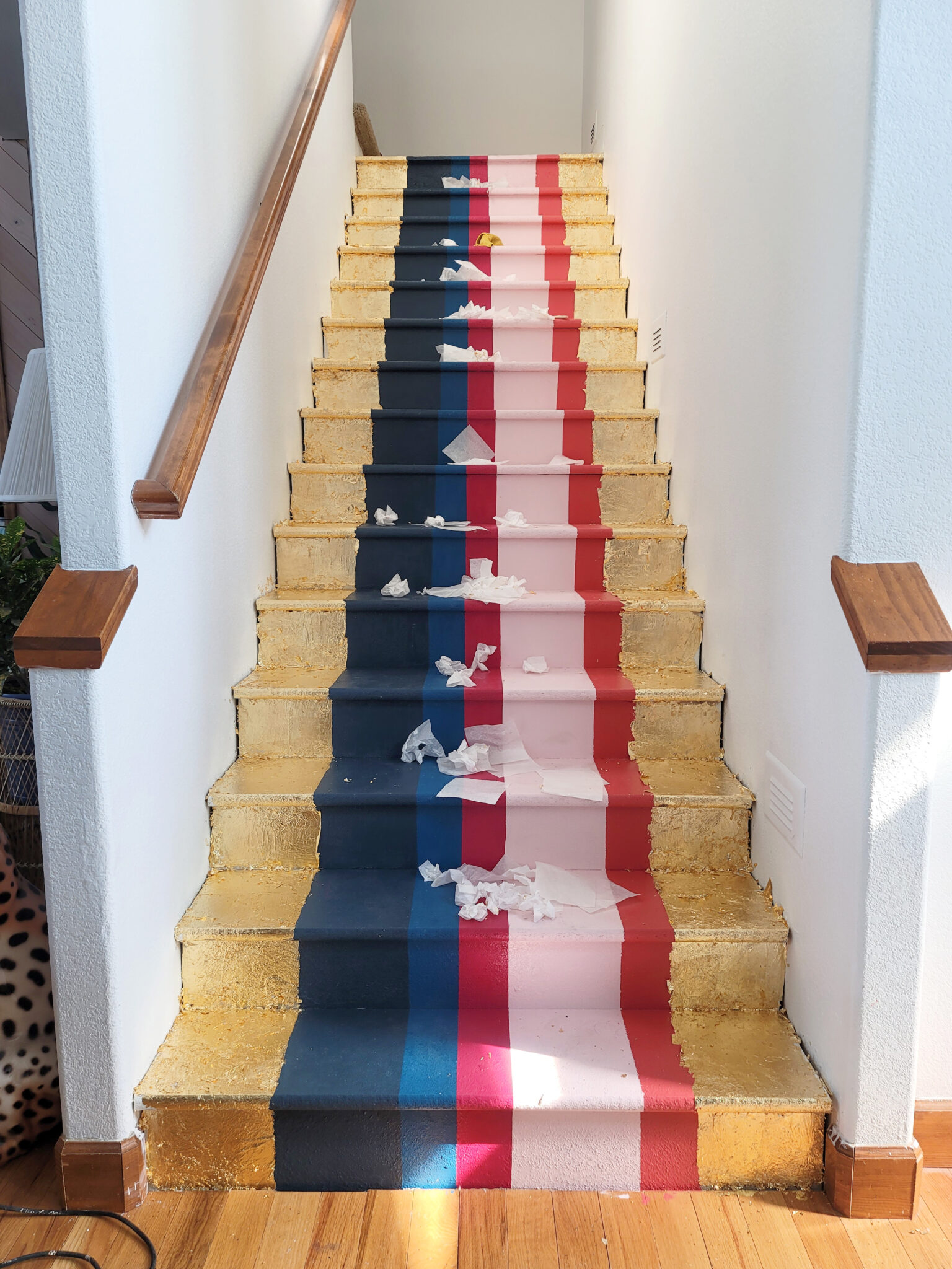 Staircase Makeover by popular CO home design blog, Eclectic Twist: image of a wooden staircase with navy blue, cobalt blue, dark pink, light pink, orange stripes and gold leafing on it. 