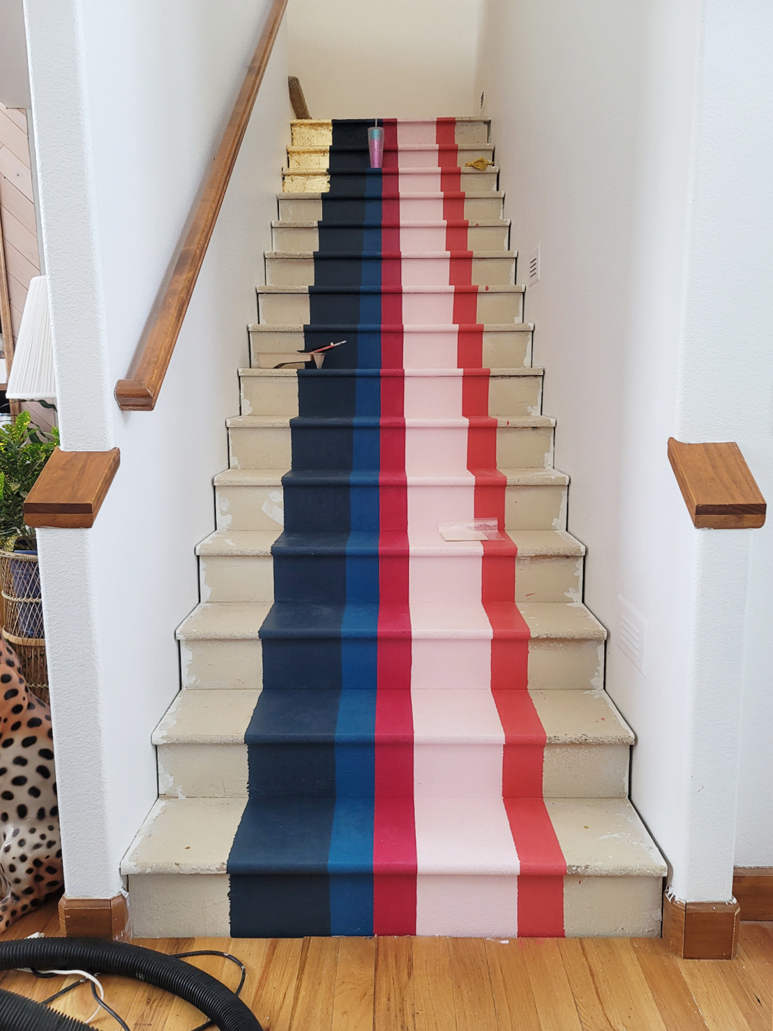 Staircase Makeover by popular CO home design blog, Eclectic Twist: image of a wooden staircase with navy blue, cobalt blue, dark pink, light pink, orange stripes and gold leafing on it. 